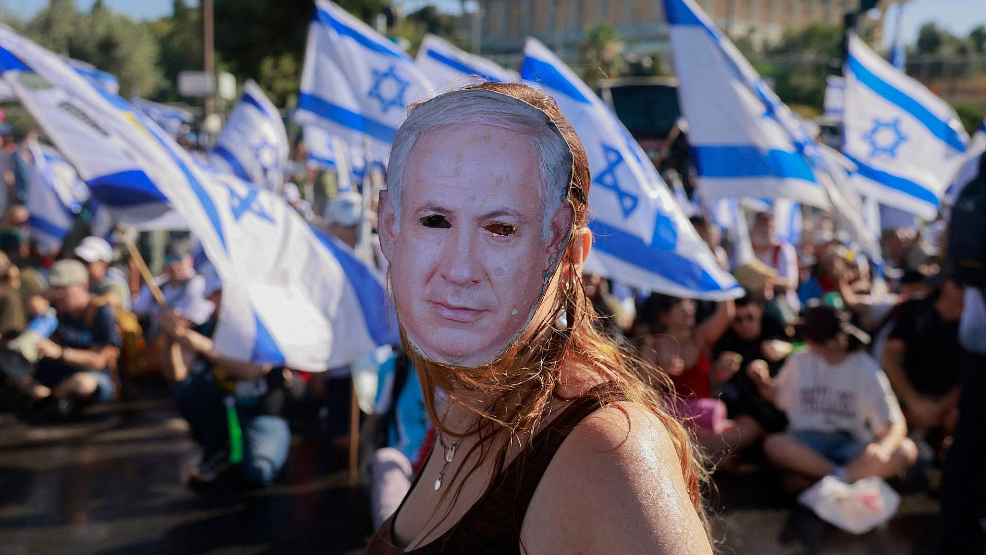 מפגינה במסכה ליד הכנסת, 24.7.23 (צילום: מנחם כהנא/AFP/גטי אימג'ס)