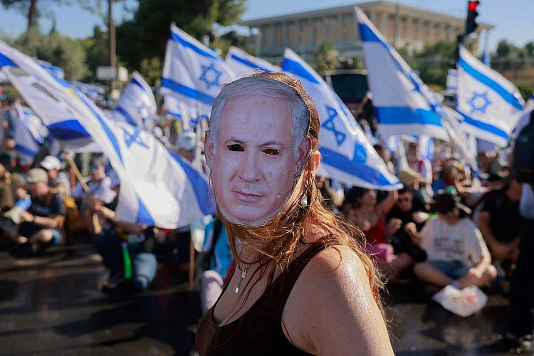 מפגינה במסכה ליד הכנסת, 24.7.23 (צילום: מנחם כהנא/AFP/גטי אימג'ס)